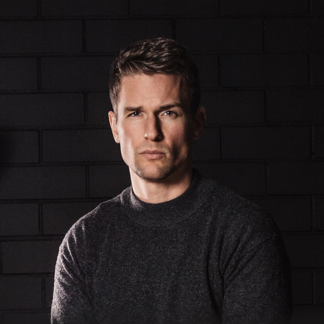 Flo Felter, founder and CEO of cosmos™, in front of a dark brick wall.